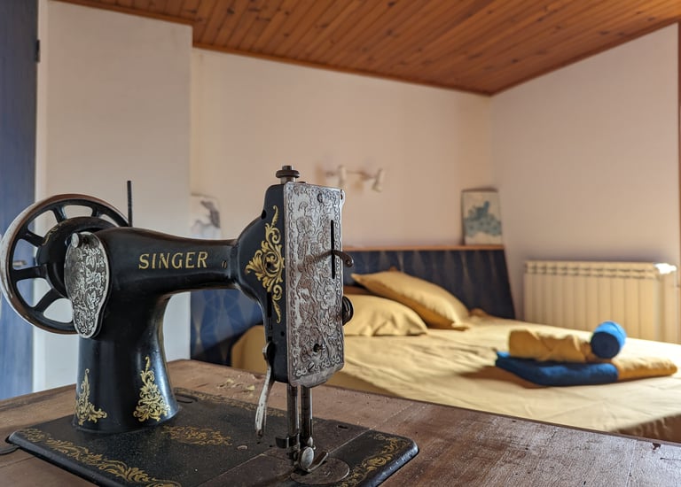 Une machine à coudre singer et en arrière plan un lit avec des draps dorés