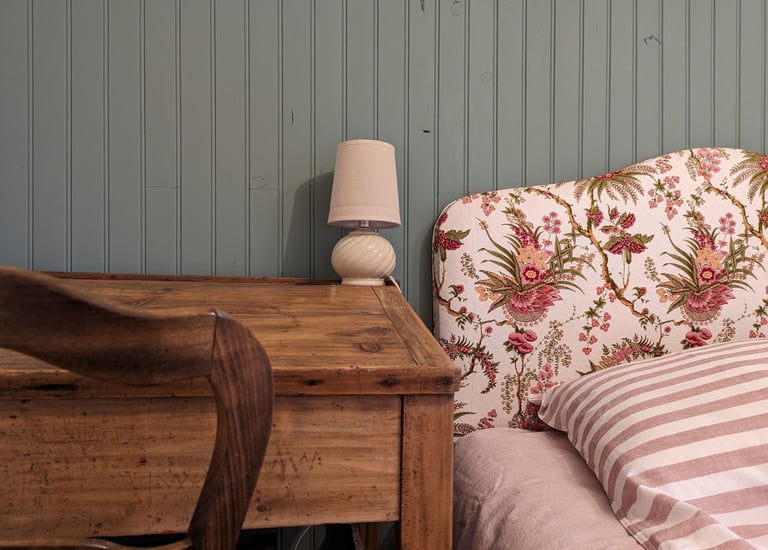 un lit avec une literie rayée, une tête de lit fleuri et un bureau d'écolier avec une lampe