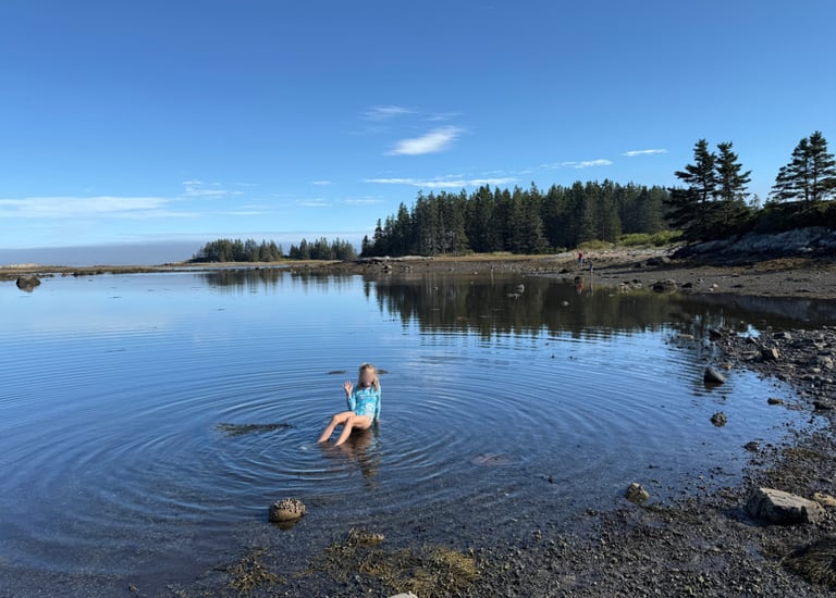 A girl sitting in a shallow tide pool along the coast of Maine at Acadia National Park