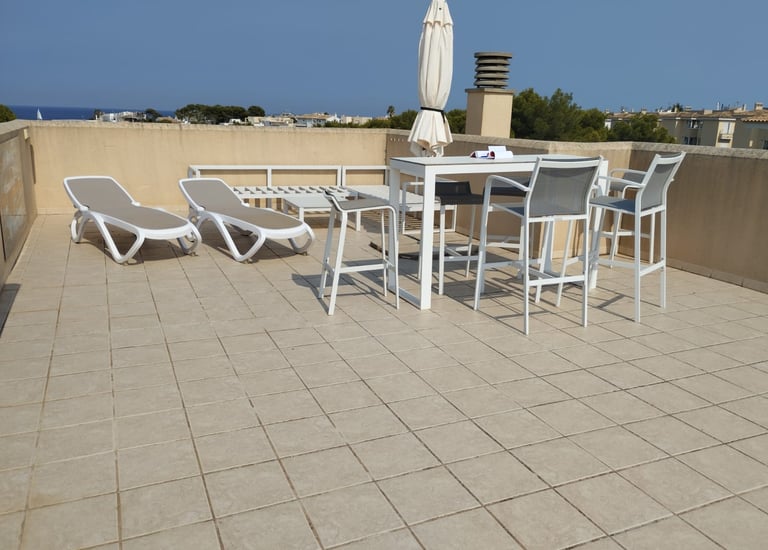 Modern rooftop terrace featuring white outdoor furniture, sun loungers, and a dining table with a sea view.