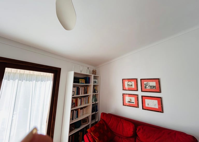 Red sofa and white bookshelf in a bright living room with framed wall art.