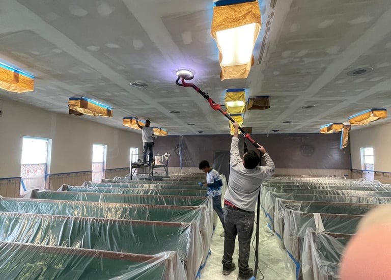 man preparing a ceiling to be painted with a sander in his hand.
