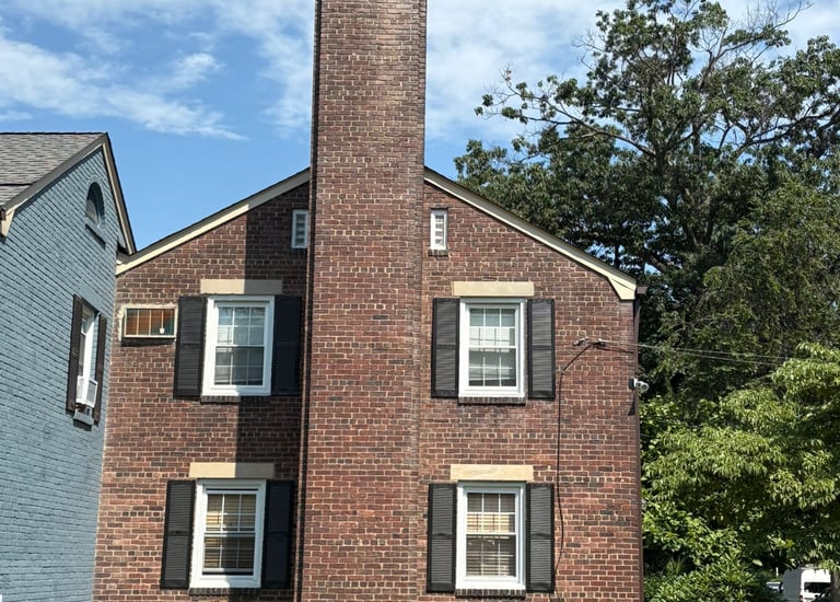 A tall, outdoor brick chimney on a house in Roslyn, New York, undergoing inspection for a major rebuild and repair project by