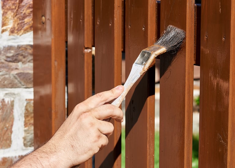 Une personne applique une protection pour bois sur une clôture de jardin et un portail