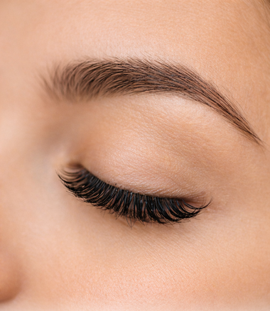 Close-up of a woman's eye with professional eyelash extensions and shaped brown eyebrows.