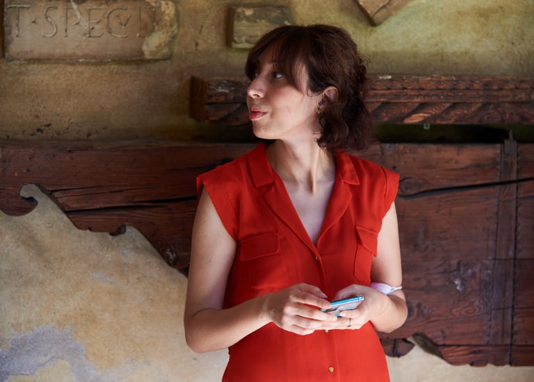 Persona con vestito rosso estivo e smartphone davanti a muro rustico in Museo
