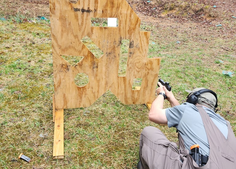Kneeling man engaging targets from a barrier using self-defense firearm during training.