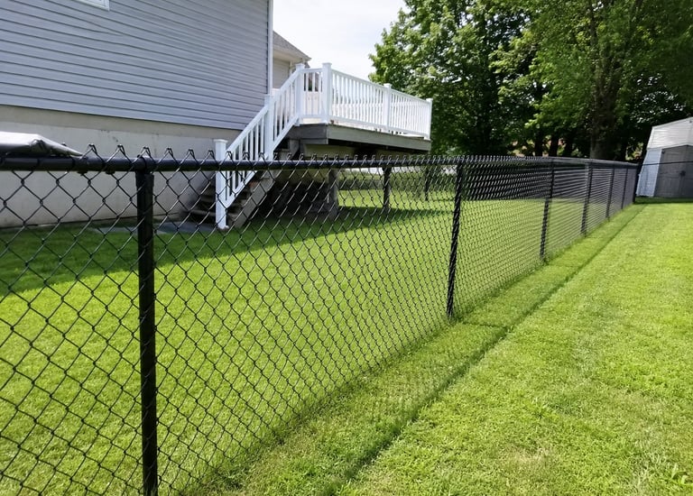 Black vinyl-coated chain link fence installed in a residential backyard with a green lawn and white deck.