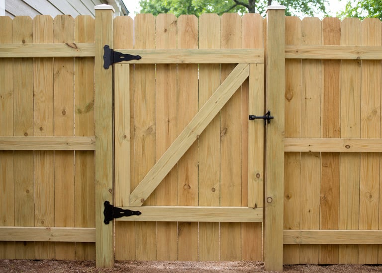 New pressure treated wood privacy fence with a matching garden gate and black metal hardware.
