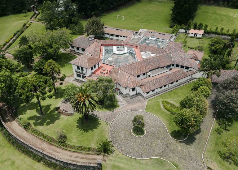 Fotografía con dron de mansión colonial de paredes blancas con techo naranja, cúpulas rodeada de naturaleza Quito Ecuador