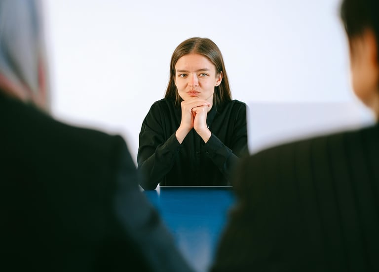 Jeune femme en entretien d'embauche face à des recruteurs, mains jointes sur la table.