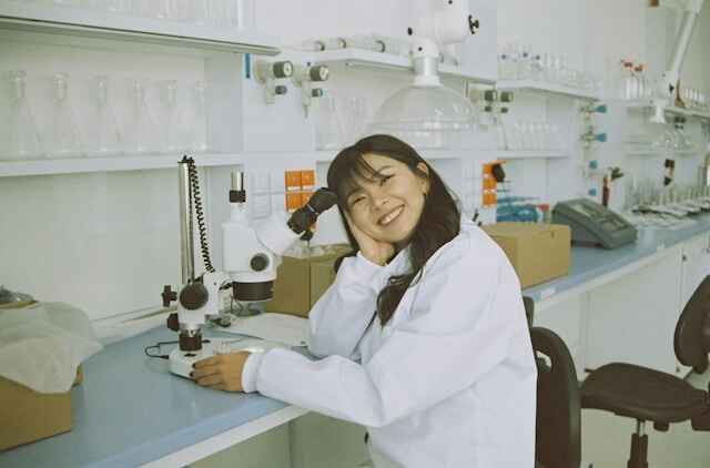 female in lab coat sitting at a desk and using a scientific microscope