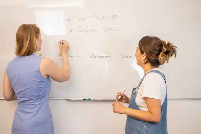 2 women writing on a white board 