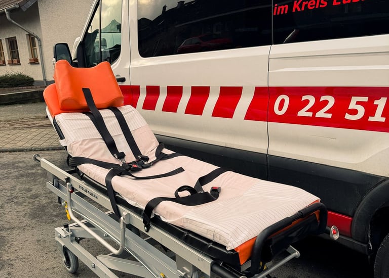 Trage mit orange Kopfstütze vor Krankenwagen mit roten Streifen und Nummern.