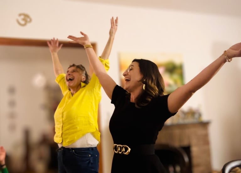 zwei Frauen lachen und singen, die Arme in der Höhe, im Hintergrund ein OM-Zeichen