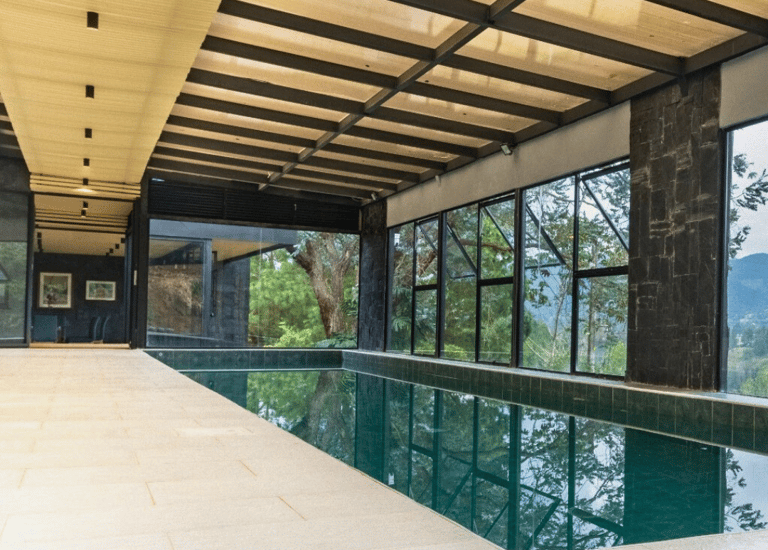 Piscina cubierta rodeada de ventanales, estructura metálica visible y cielo raso de madera.