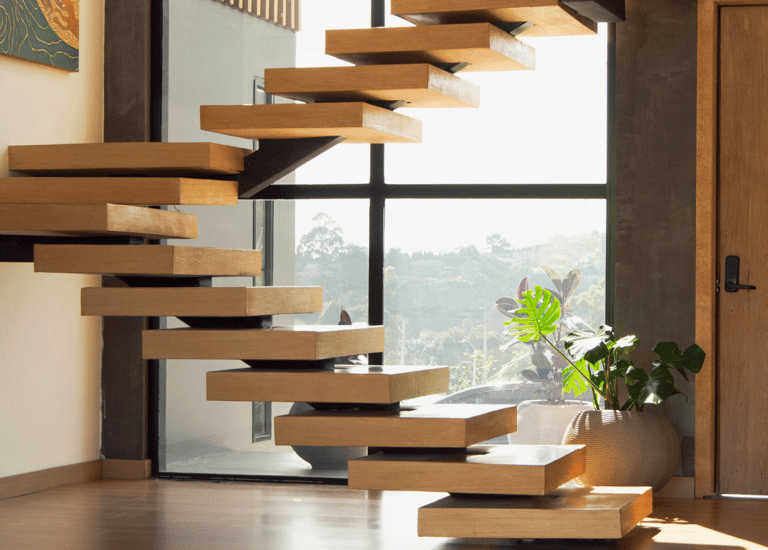 Escalera interior flotante de madera con estructura metálica y fondo acristalado.