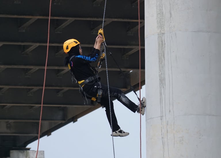 Professional bridge inspector rappelling on ropes to perform maintenance on a concrete pillar.