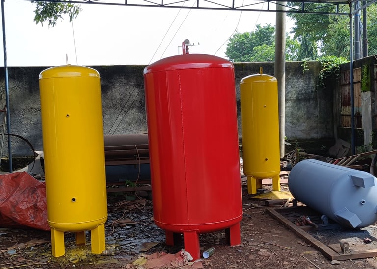 Industrial air compressor receiver tanks in red and yellow at a manufacturing workshop.