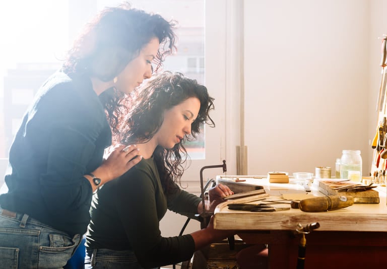 Dos artesanas mujeres trabajando con joyería en un taller luminoso.