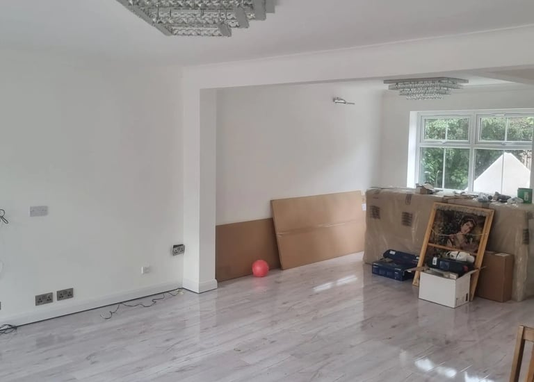 Empty living room featuring grey laminate flooring, white walls, and a modern crystal chandelier light fixture.