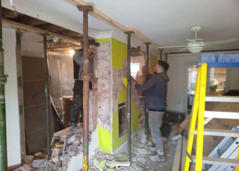 Construction workers using steel acrow props for structural support during a home wall demolition.
