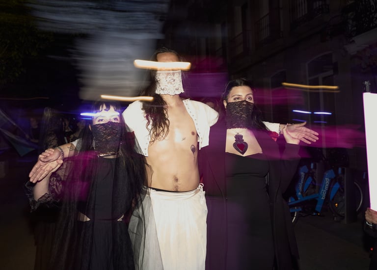 Performers in gothic avant-garde costumes and lace face veils pose during a nighttime city street event.