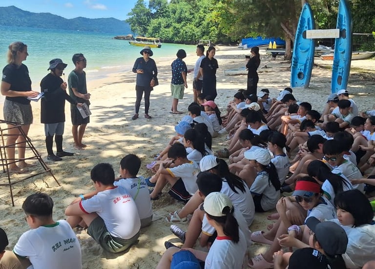 a group of students sitting on a beach during coral planting program