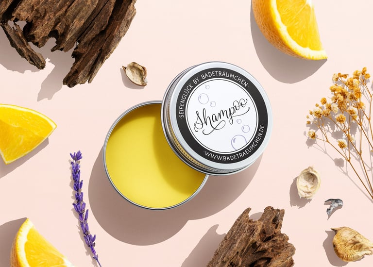 Natural solid shampoo bar in a tin surrounded by fresh orange slices, lavender, and wood.