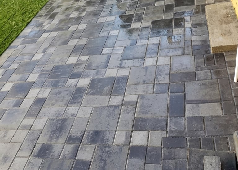 Backyard patio installation with interlocking grey stone pavers next to a lush green lawn, showcasin