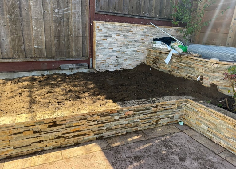 Raised garden bed featuring stacked stone retaining walls filled with fresh dark topsoil.