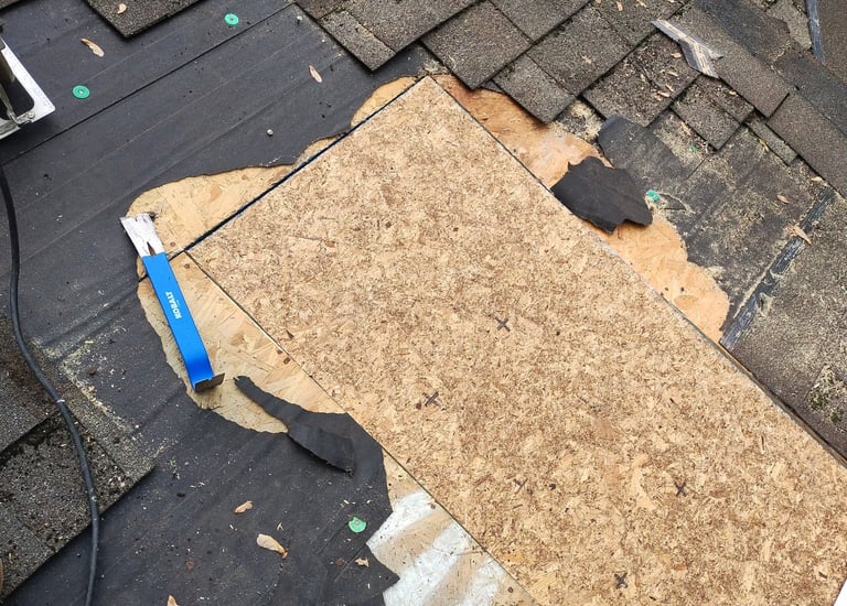 Roofing contractor replacing damaged asphalt shingles and repairing wood roof decking with tools.