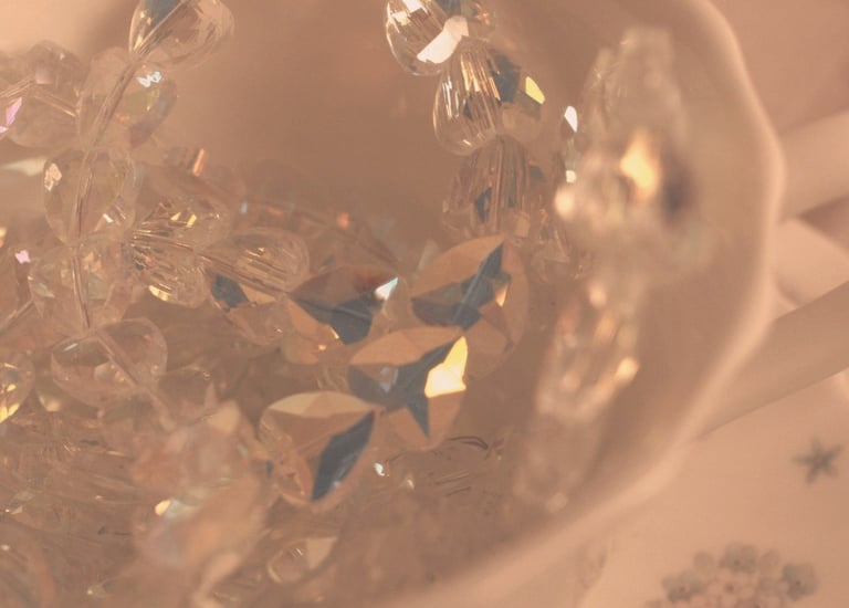 Elegant crystal beads and iridescent glass jewelry inside a vintage porcelain teacup with soft aesthetic lighting.