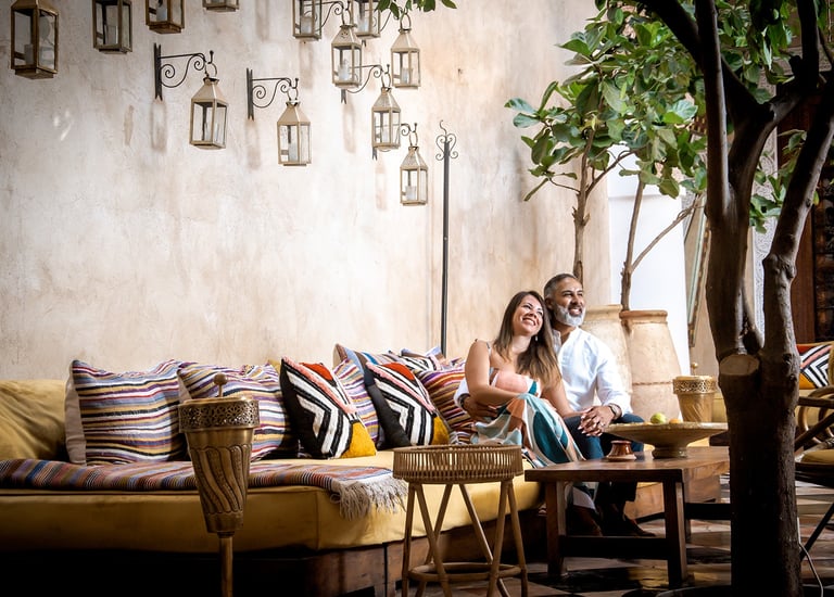 Smiling couple relaxing on a Moroccan-style lounge with colorful pillows and hanging lanterns.