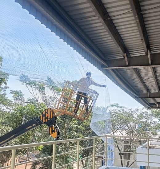 Technician carefully installing pigeon nets on a high-rise balcony.