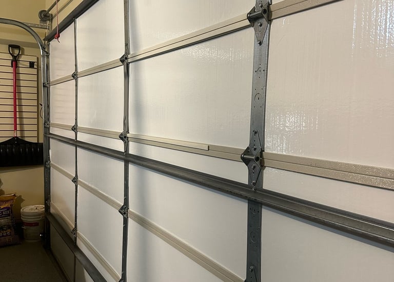 Interior view of an insulated sectional white garage door with metal hinges and tracks.