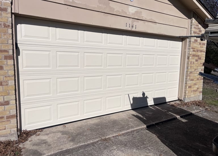 Almond sectional garage door installation on a residential brick house driveway.
