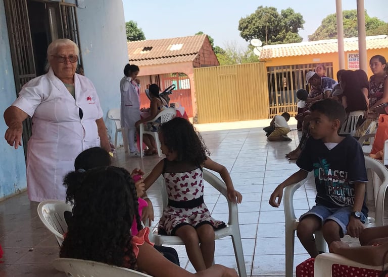 A healthcare worker in a white uniform assists children at a community health clinic in Brazil.
