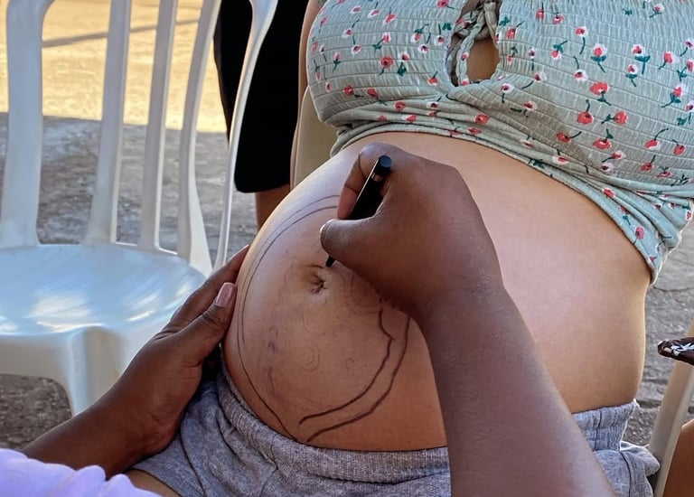 Artist drawing a creative design with a marker on a pregnant woman's belly outdoors.