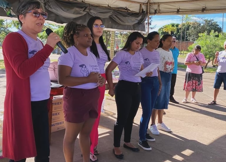 A group of women in purple shirts presenting at a community health event about maternal care.