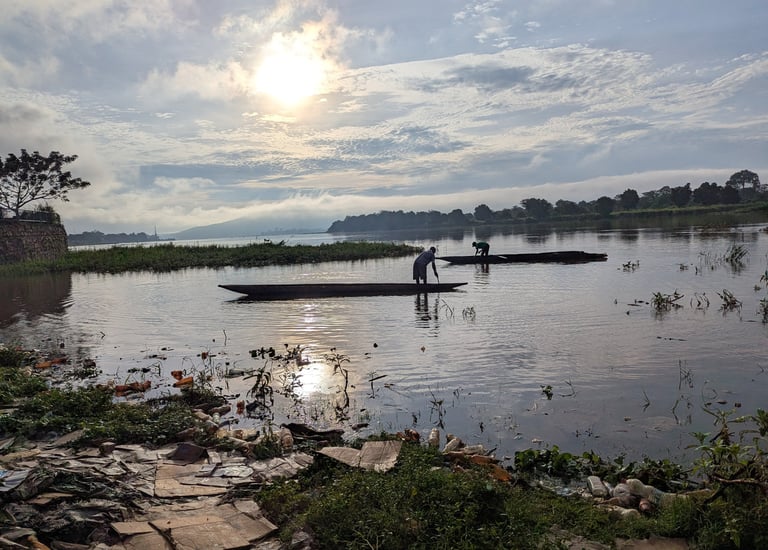 Fishermen in wooden dugout canoes on a river during a bright sunrise with plastic pollution in the foreground.