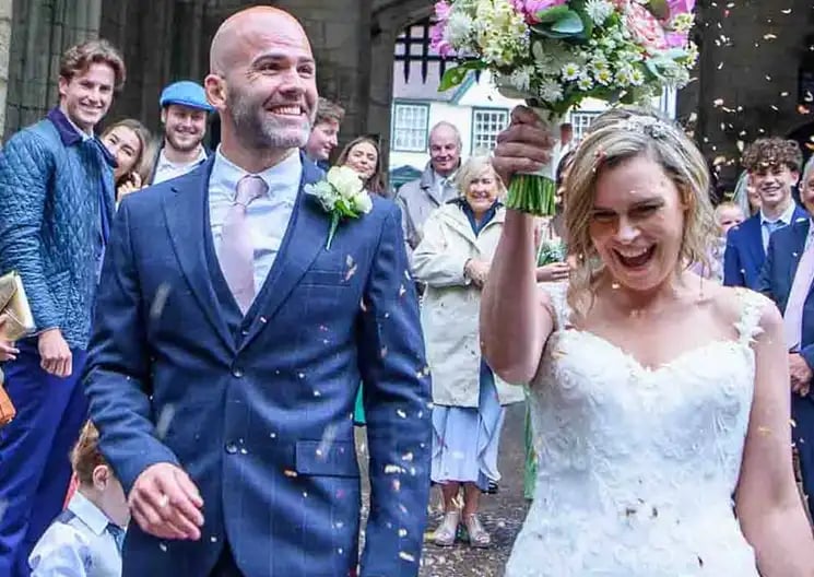 Smiling bride and groom celebrate under falling confetti during their outdoor wedding ceremony.