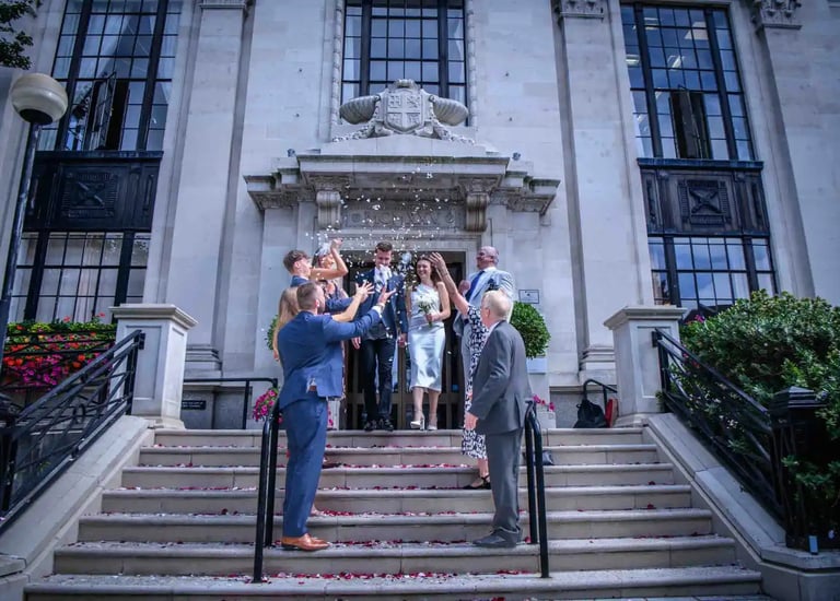 Newlywed couple exits Islington town hall while guests throw white confetti on the stone steps.