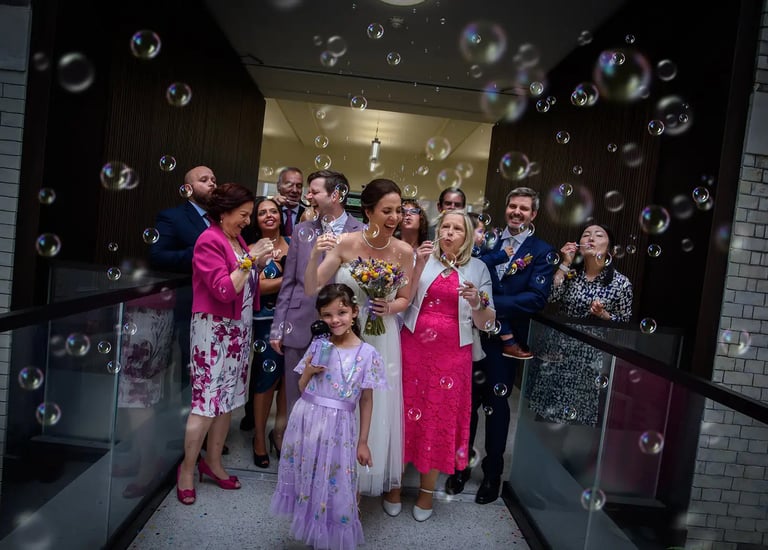 Wedding guests blow bubbles around a smiling bride and groom during a joyful exit celebration.