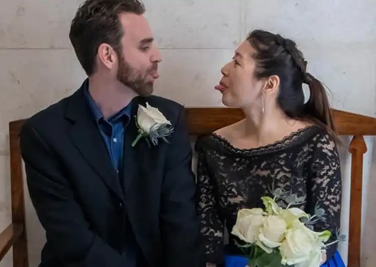 A playful bride and groom making funny faces while sitting together at their wedding venue.