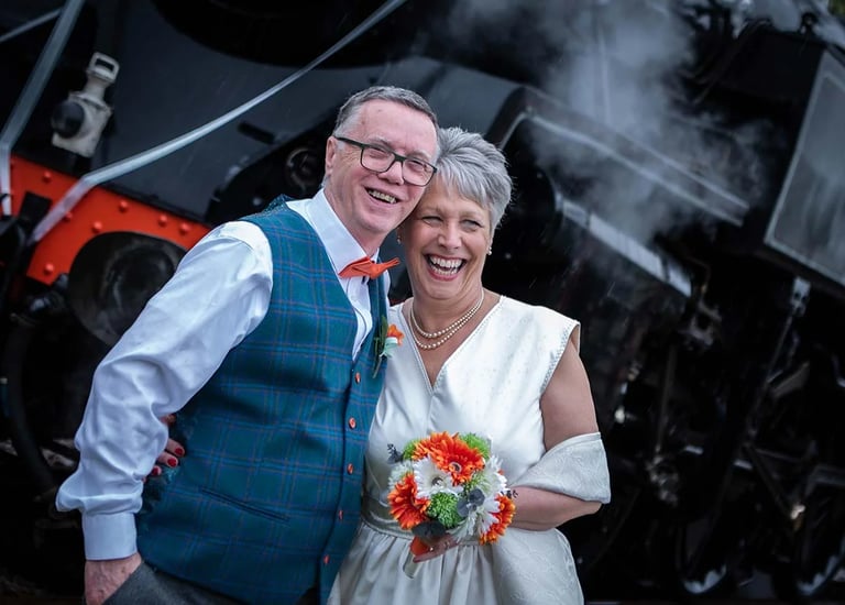 bride and groom standing in front of a steam train