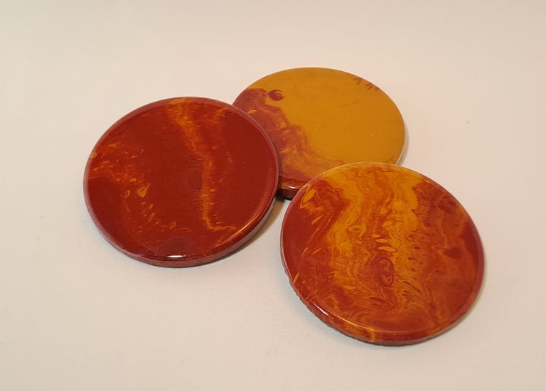 Three round handmade resin coasters featuring marbled red and yellow earth tone patterns.