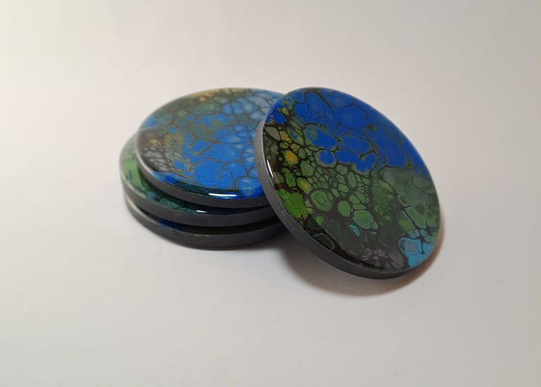 Handmade round drink coasters with blue and green fluid art resin cells.
