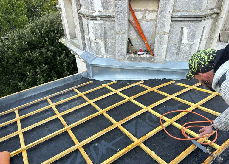 Un couvreur professionnel installe des liteaux en bois sur une membrane étanche sur le toit d'un bât