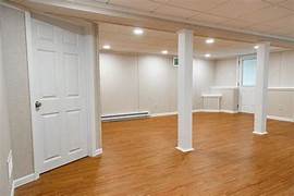 Spacious finished basement featuring wood laminate flooring, recessed lighting, and white support columns.